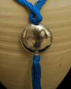 Detail of art déco pendant necklace in turquoise and a hammered silver sphere with hanging tassel on a black backdrop