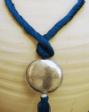 Detail of art déco pendant necklace in petrol blue and a hammered silver sphere with hanging tassel on white backdrop