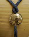 Detail of art déco pendant necklace in grey blue and a hammered silver sphere with hanging tassel on white backdrop