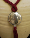 Detail of art déco pendant necklace in light bordeaux and a hammered silver sphere with hanging tassel
