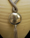 Detail of art déco pendant necklace in taupe and a hammered silver sphere with hanging tassel