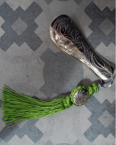 Hand engraved silver shoehorn with decorative tassel in pistachio green shown on a grey decorative Spanish tile @ Andaluchic