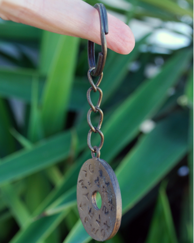 Flat donut keyring handmade in copper & engraved with phoenician alphabet shown hanging from a finger