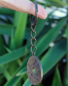 Llavero de redondo plano hecho a mano en cobre y grabado con el alfabeto fenicio que cuelga de un dedo