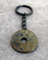 Vue de face d'un porte-clés plat et rond fait à la main en cuivre et gravé de l'alphabet phénicien sur un carreau de terre cuite