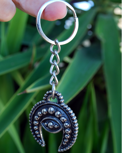 Front view of a handmade white copper crescent moon evil eye phoencian keyring shown hanging from a finger