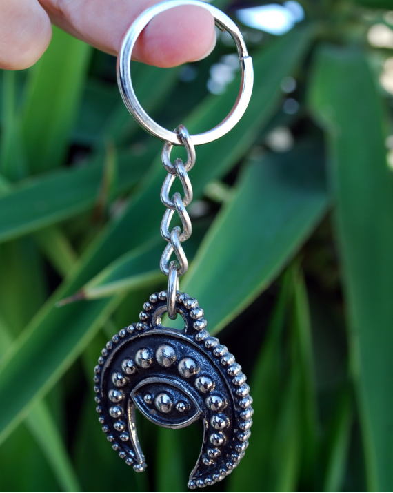 Front view of a handmade white copper crescent moon evil eye phoencian keyring shown hanging from a finger