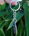 Side view of a handmade white copper crescent moon evil eye phoencian keyring shown hanging from a finger