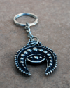 Flat front view of a handmade white copper crescent moon evil eye phoencian keyring displayed on a terracotta tile