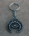 Bird´s eye view of a handmade white copper crescent moon evil eye phoencian keyring displayed on a terracotta tile