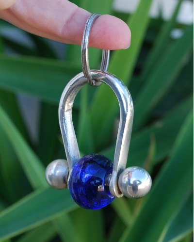Versilberter Kupfer-Schlüsselanhänger mit blauer Glasperle, das an einem Finger baumelt