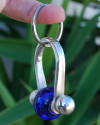 Side view of royal blue glass ball keyring on chunky silvered copper for him or for her shown to size dangling from a finger