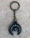 Front view of a handmade copper phoencian keyring with a motif of a crescent moon combined with evil eye